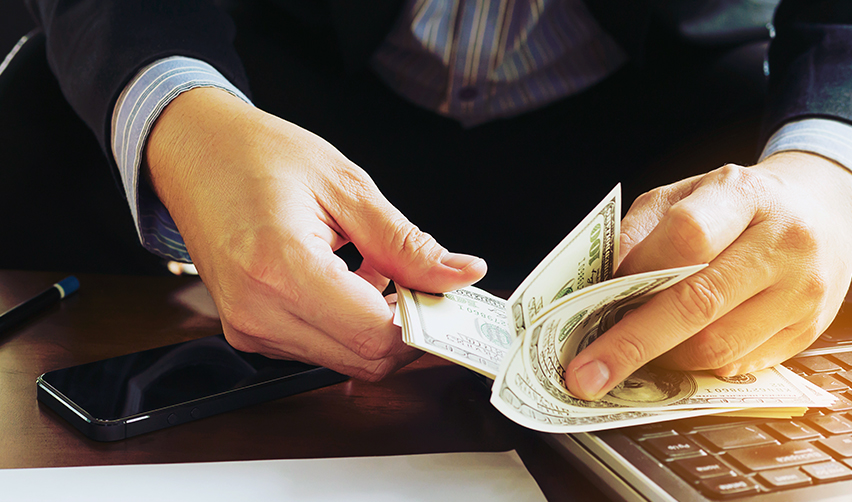 An investor counts how much capital he has available. His smartphone and laptop are also visible.