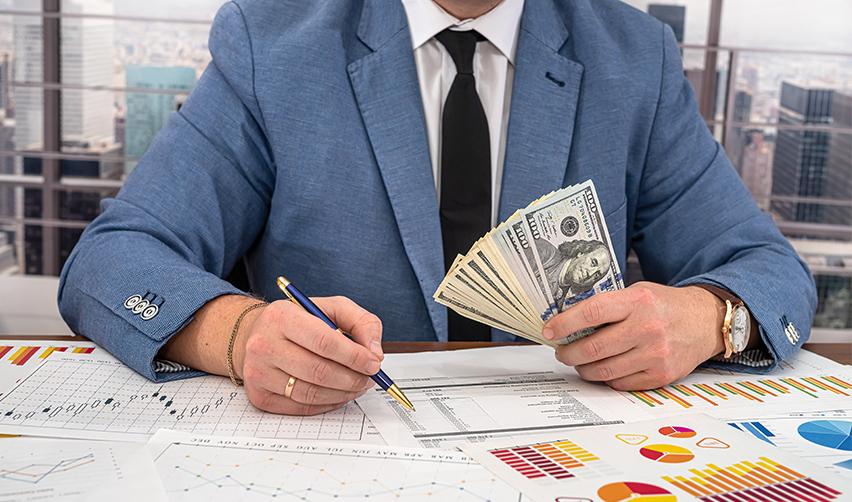 An EB5 investor working on an existing business plan while holding a stack of dollars.