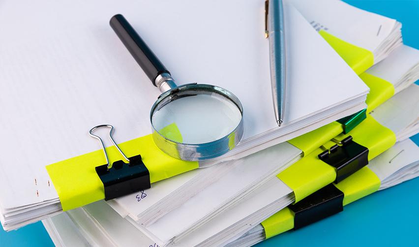 A magnifying glass on a stack of supporting documents to prove lawful source of funds along with the I 526 petition.