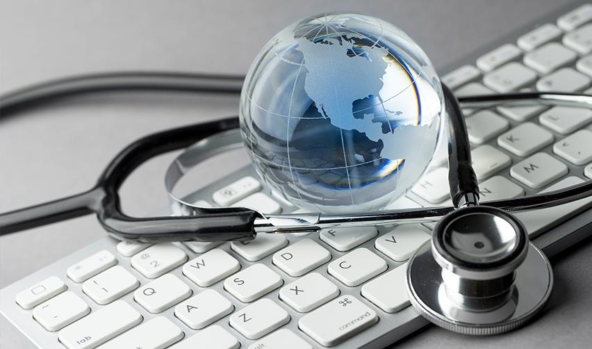A stethoscope around a mini globe on top of a keyboard, concept for global healthcare.