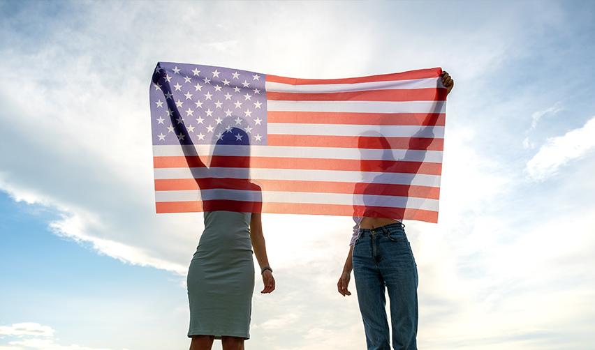 Two women who completed their U.S. visa registration process holding up an American flag.