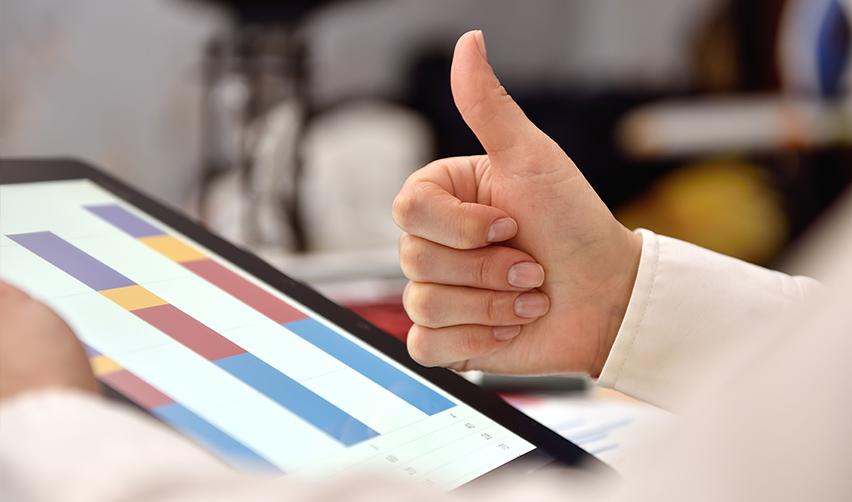 A hand giving a thumbs up in front of a screen with immigrant investor capital graphs on it.