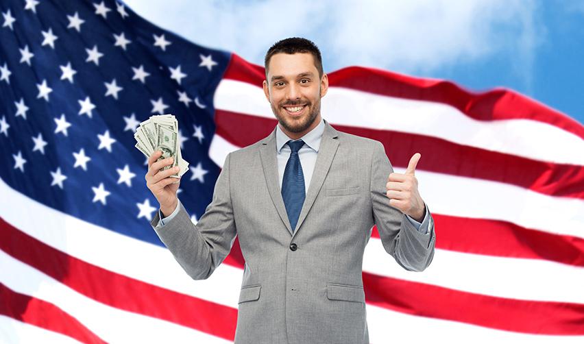 An immigrant investors EB 5 minimum investment funds in one hand, and a thumbs-up on the other, standing in front of an American flag.