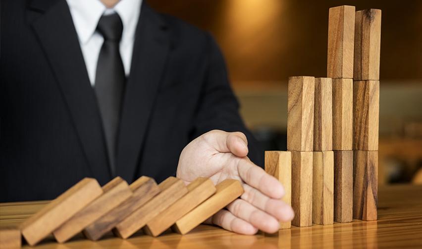 A hand stopping a domino effect, symbolizing low-risk projects.