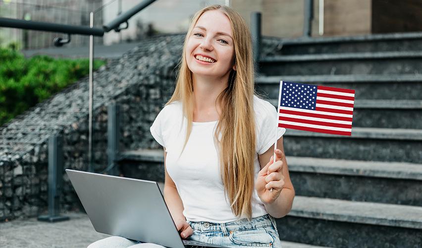 A person holding an American flag with a laptop on her lap, registering for an H1B visa through her USCIS online account.