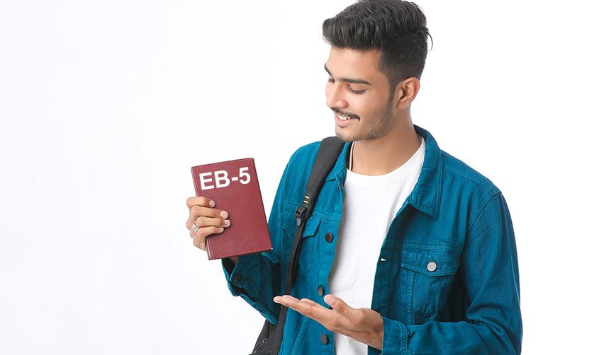 A person holding a passport that says EB-5 on it, referring to the EB-5 visa Indian investors pursue.