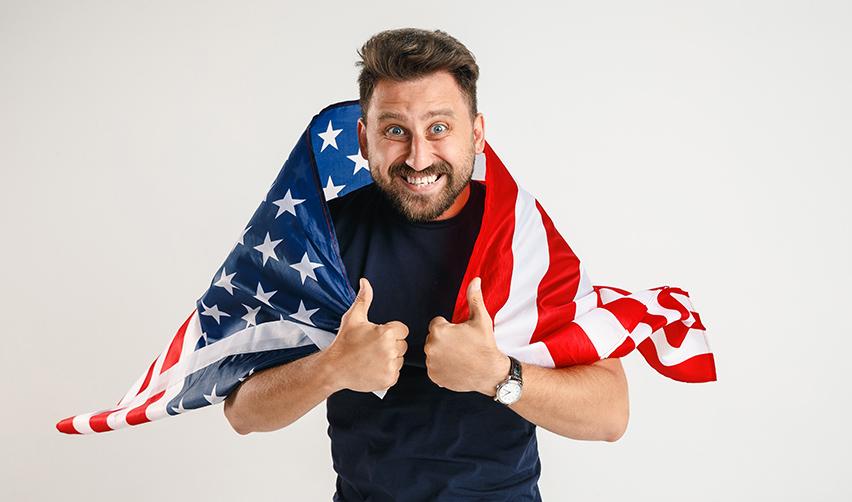 A Green Card holder holding an American flag and giving two thumbs up.
