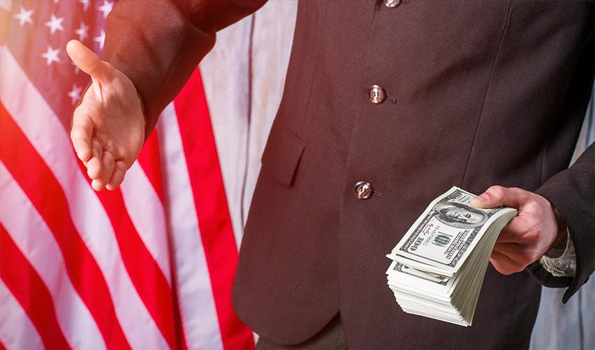 A person holding a bundle of money and reaching out for a handshake in front of the U.S. flag.