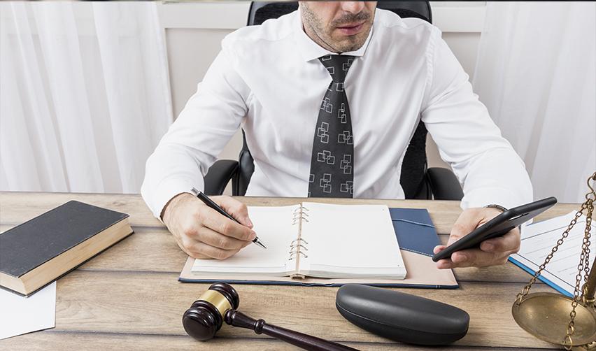 An immigration attorney sitting at his desk in his office, looking at his phone and taking notes.