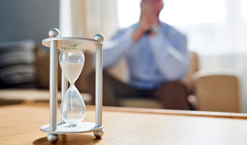 A close-up of an hourglass symbolizing I-485 processing times, with the silhouette of a frustrated applicant in the background.