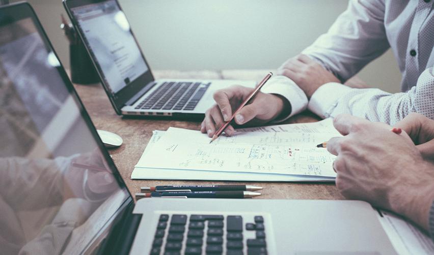 A close-up of hands taking notes on pieces of paper on a desk and working together on low-risk EB-5 projects.