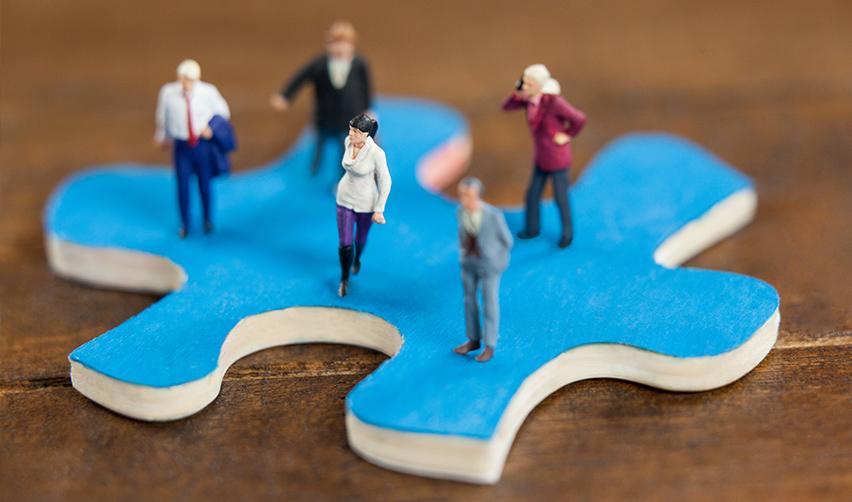 Figurines of green card applicants standing on a jigsaw puzzle piece.