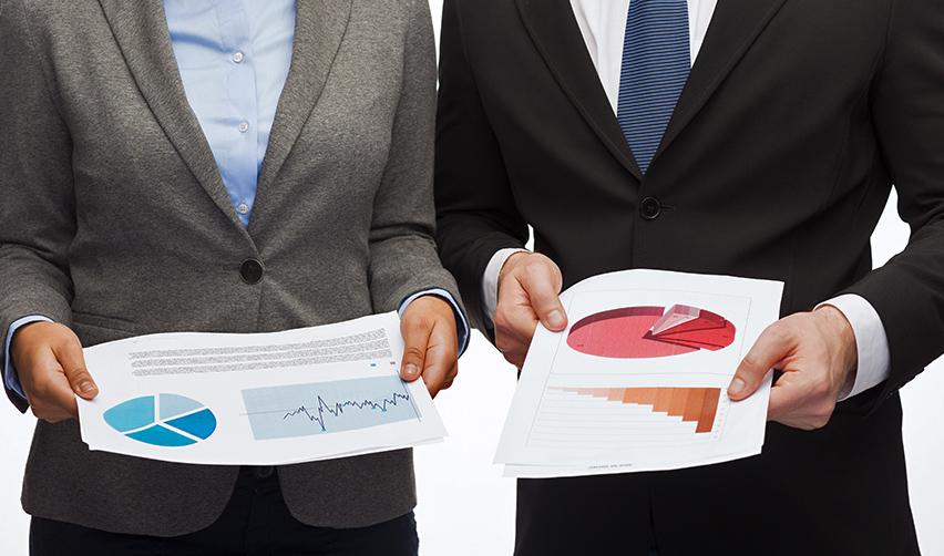 Two foreign investors holding documents with business data and pie charts on them.