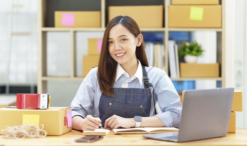 A student sitting at a desk in front of a computer, writing on a notepad.