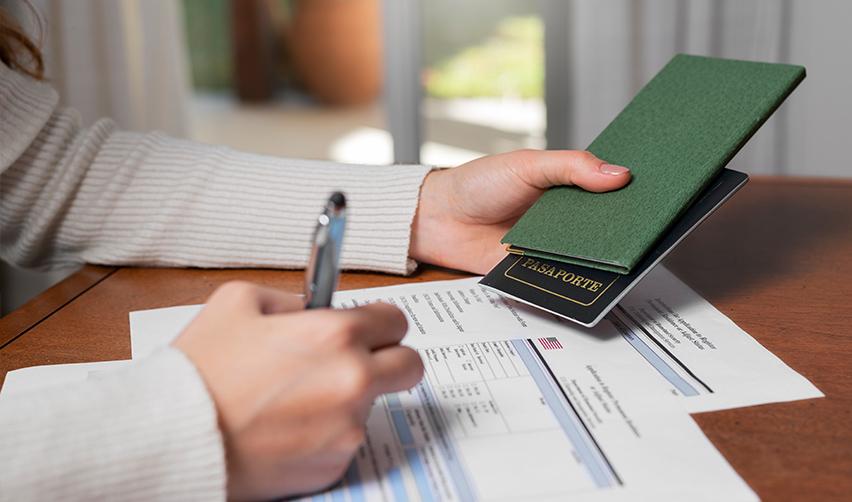 A person filling out a visa application form with a passport and a pen in her hand.