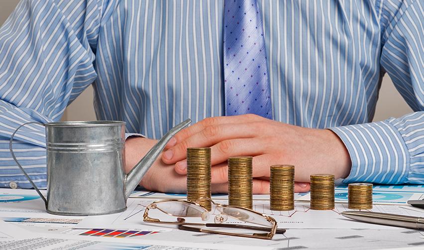 A person sitting at a desk with stacked coins and investment graphs on it.