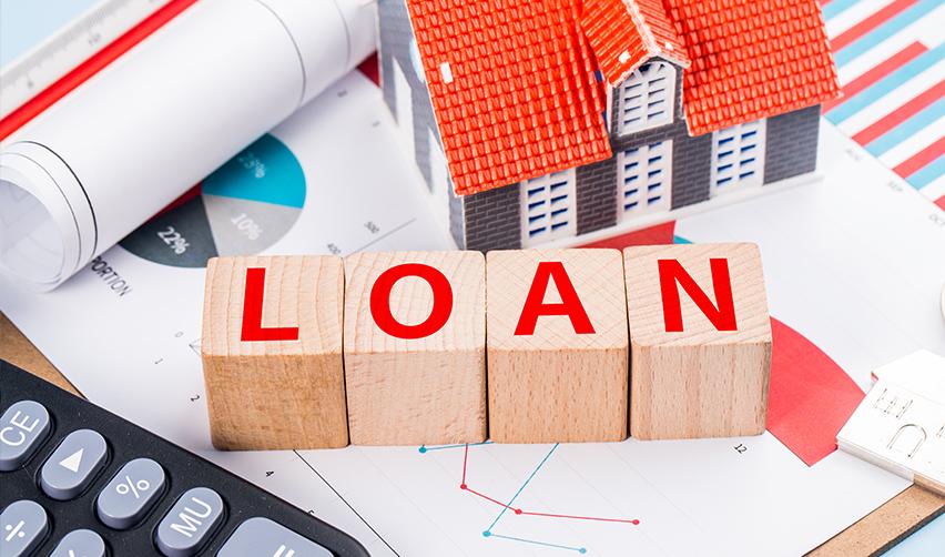 Wooden blocks with red letters reading loan, on a loan agreement and business documents with a model house and calculator.