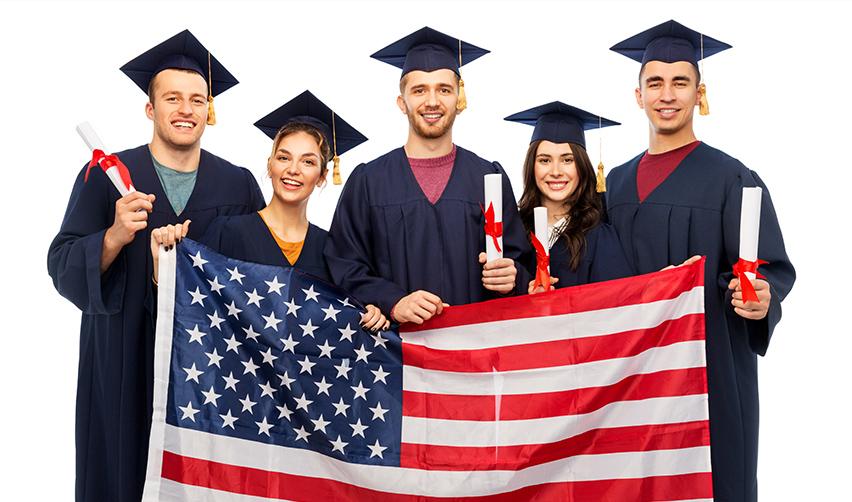 A group of F1 students in graduation gowns and caps holding an American flag.