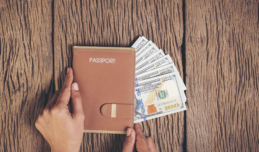 A hand holding a passport with some money inside, representing a capital investment for an EB-5 visa.