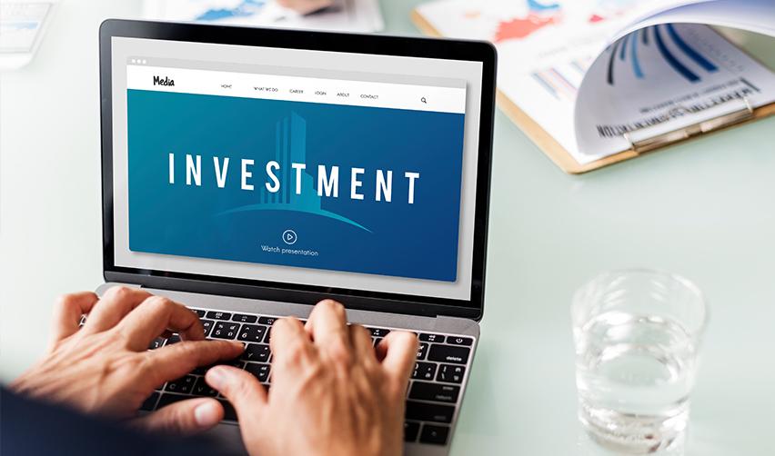 A person using a laptop on a desk, with the word investment on the screen.