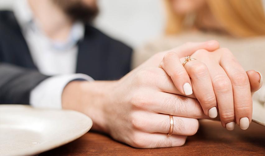 A close up of a couple hands holding with wedding bands on their fingers.
