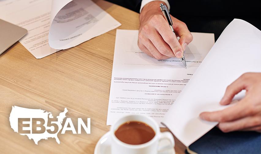 A person signing a contract or an escrow agreement on a desk, with the EB5AN logo on the side.