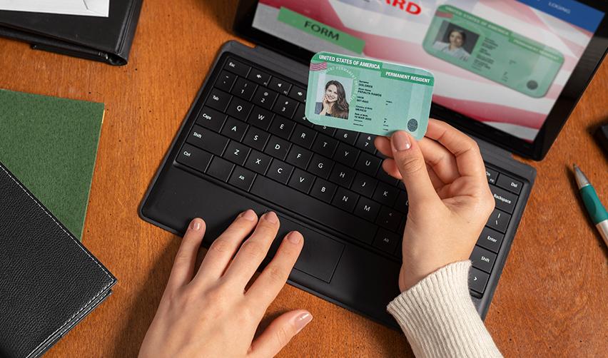 A person holding a Green Card in her hand while filling out an application form on a computer.