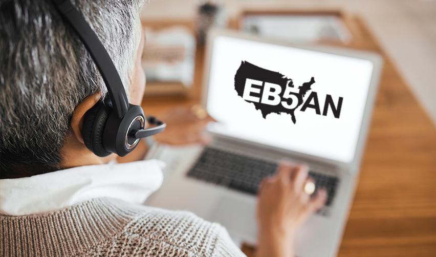 A person wearing headphones and using a computer with the EB5AN logo on the screen.