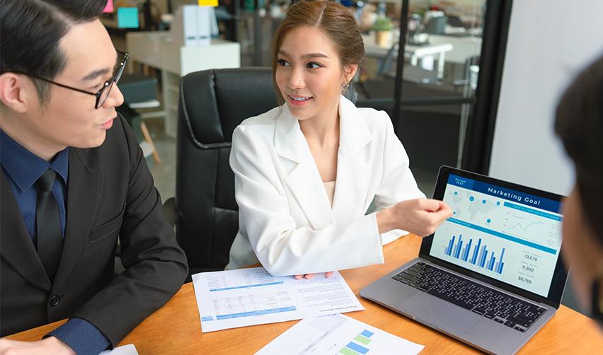 A property management company employee giving a tech worker helpful tips about his H1b investment options on a computer screen in an office.