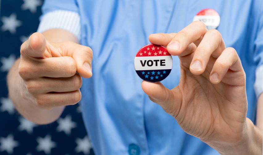 Close-up of a hand holding a badge that reads Vote, as part of the benefits of U.S. citizenship.