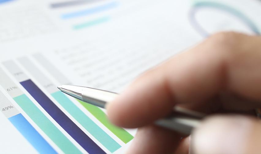 A close-up of a hand examining some business graphs and financial data.