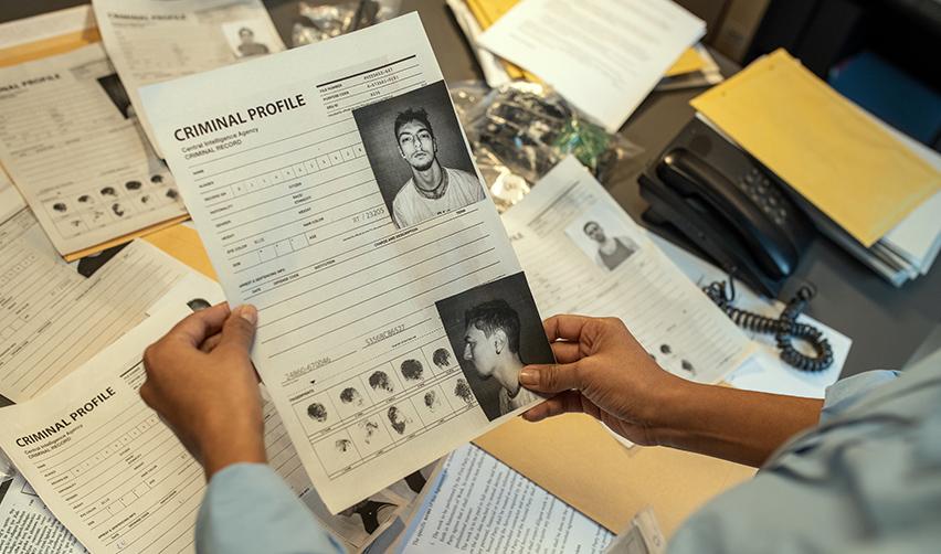 A person holding up a criminal profile over a desk and examining an EB5 applicant's criminal record.