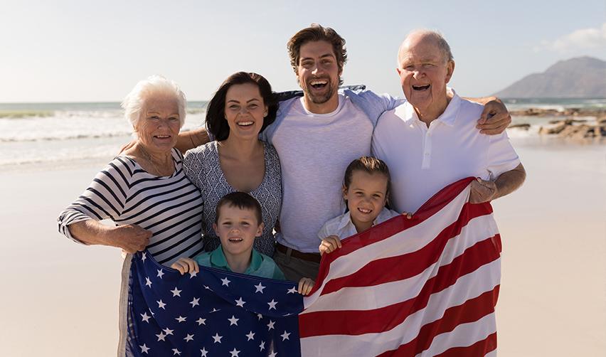 An EB5 investor and his extended family holding up an American flag at a beach after getting permanent immigration status through foreign investment funds.