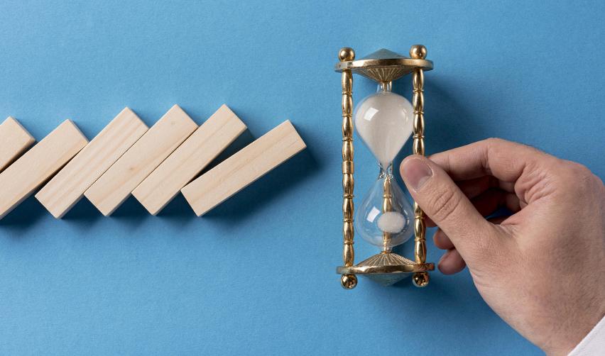 A hand holding an hourglass next to some wooden blocks, symbolizing visa backlogs and EB5 processing times.