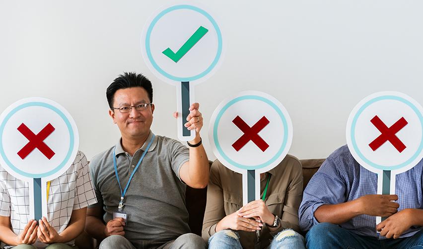 A person holding up a green check sign while others are sitting next to him with red cross signs on their faces. It symbolizes EB5 visa eligibility and who qualifies as an EB5 investor.