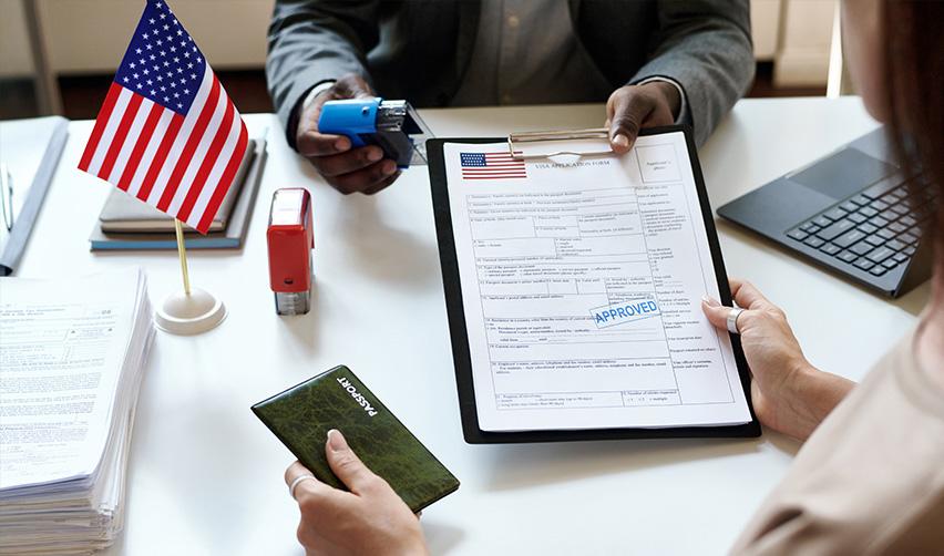 An immigration lawyer or a national visa center official handing a permanent green card application to an EB-5 investor.