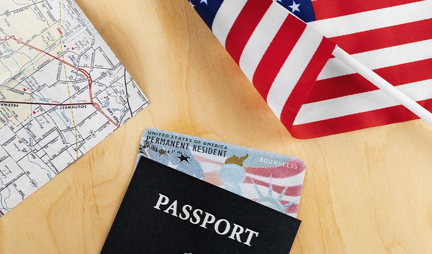 An American flag and map next to a passport with a permanent resident card (green card) in it.