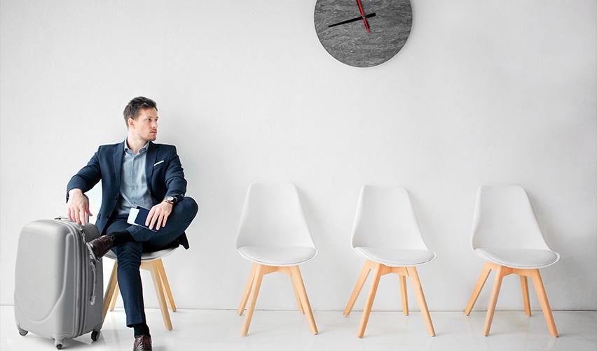 An immigrant visa category applicant waiting at a lounge with empty chairs next to him.