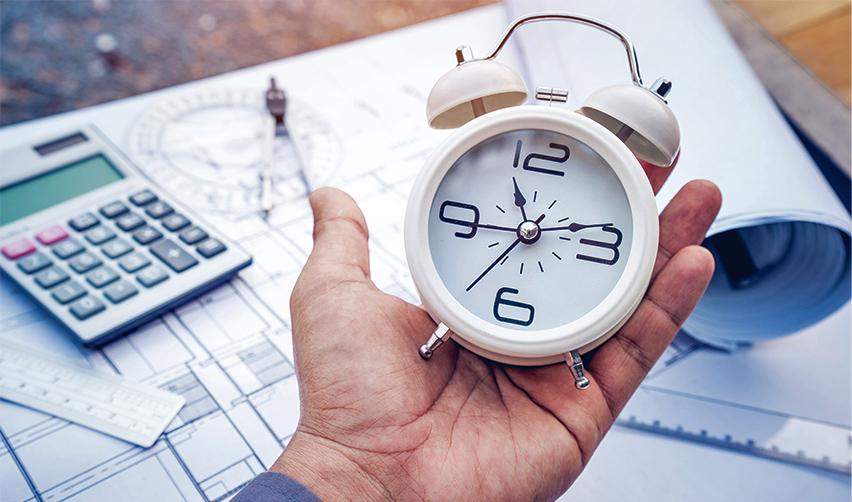 A hand holding an alarm clock against the backdrop of some EB5 project documents, symbolizing faster processing times with rural EB5 regional center investments.