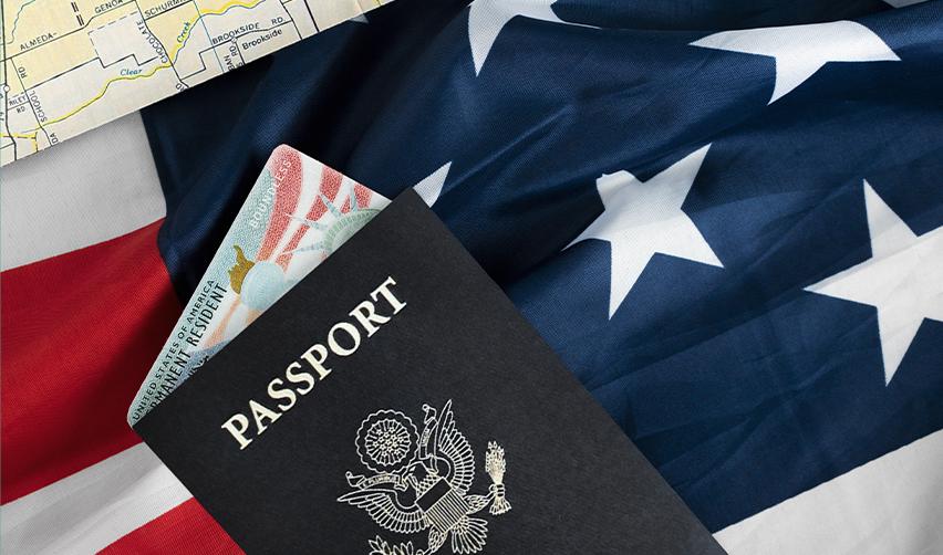 A U.S. passport and Green Card in front of an American flag.