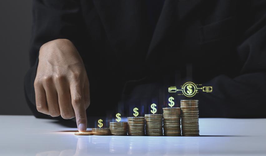Stacks of coins with digital dollar icons above them, and the hand of an EB5 alien entrepreneur touching them. Minimum capital investment requirement for the EB5 visa.