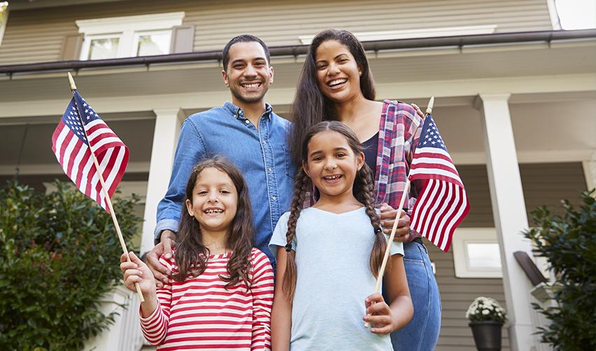A family of Eb5 investors standing in front of a house holding U.S. flags.