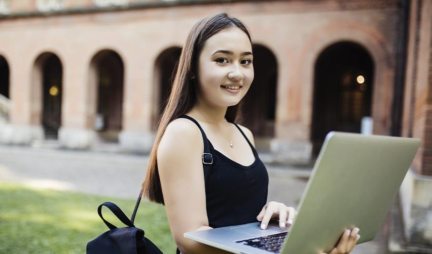 International student with a laptop on a university campus, showcasing educational benefits of the EB5 visa, including in-state tuition savings.