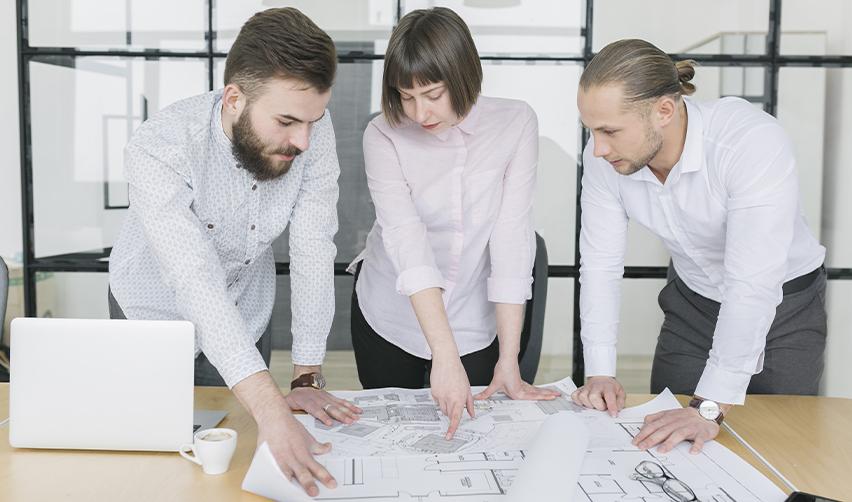 A team of regional center professionals reviewing blueprints in an office, highlighting due diligence and strong project planning as essential steps to avoid EB5 project delays.