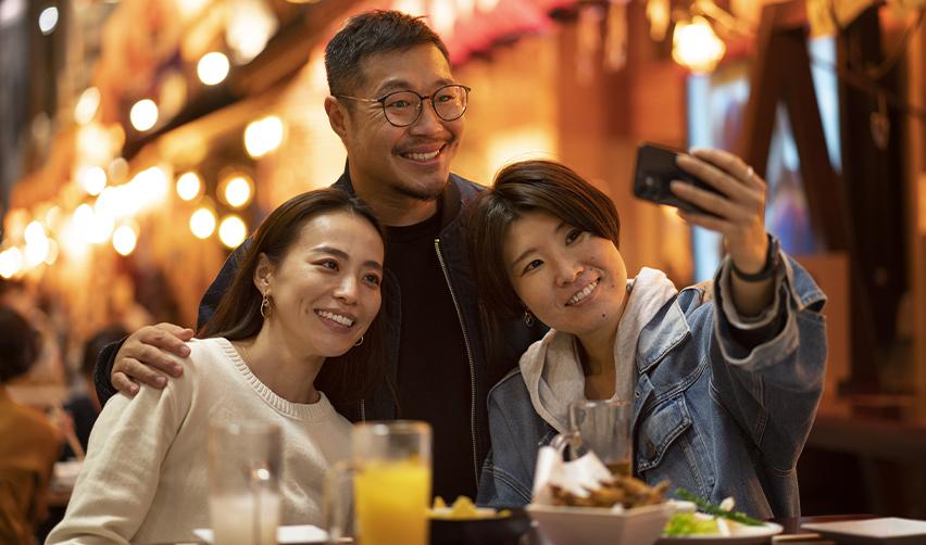 An Asian EB5 investor and two EB5 dependents taking a selfie at a restaurant.