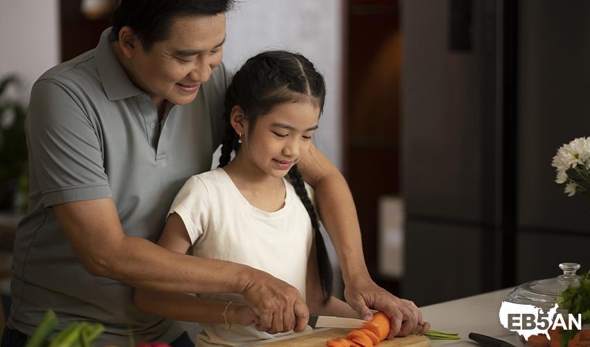 A smiling father helping his young daughter in a kitchen. This image represents families creating a secure future through the EB5 program, emphasizing opportunities for education and stability in the United States.