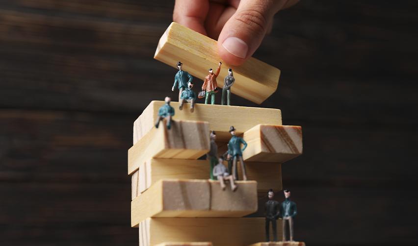 Hand stacking blocks with miniature figures representing EB5 investment success with EB5AN's help.