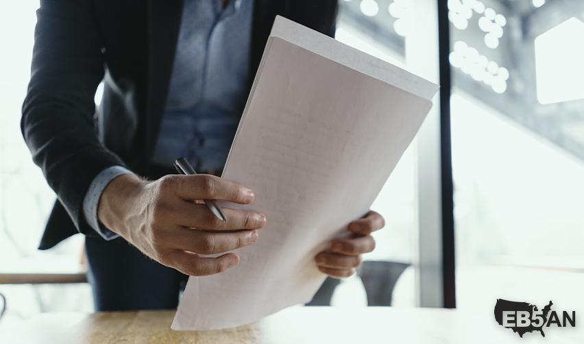 Close-up of a man holding documents, symbolizing USCIS notices like NOIDs issued during EB5 visa petition evaluations, with the EB5AN logo on the corner.