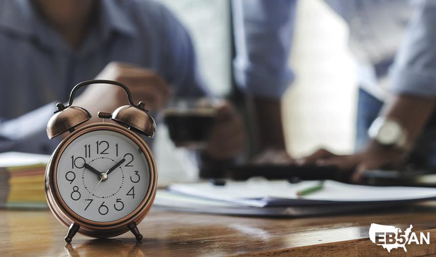 An alarm clock on an EB5 regional center principal's desk with the EB5AN logo on the corner, symbolizing faster processing times with EB-5 rural TEA projects.