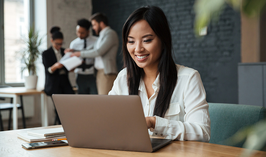 Smiling professional woman working on a laptop in a modern office, representing the EB5 visa as an investment-based pathway to US permanent residency.